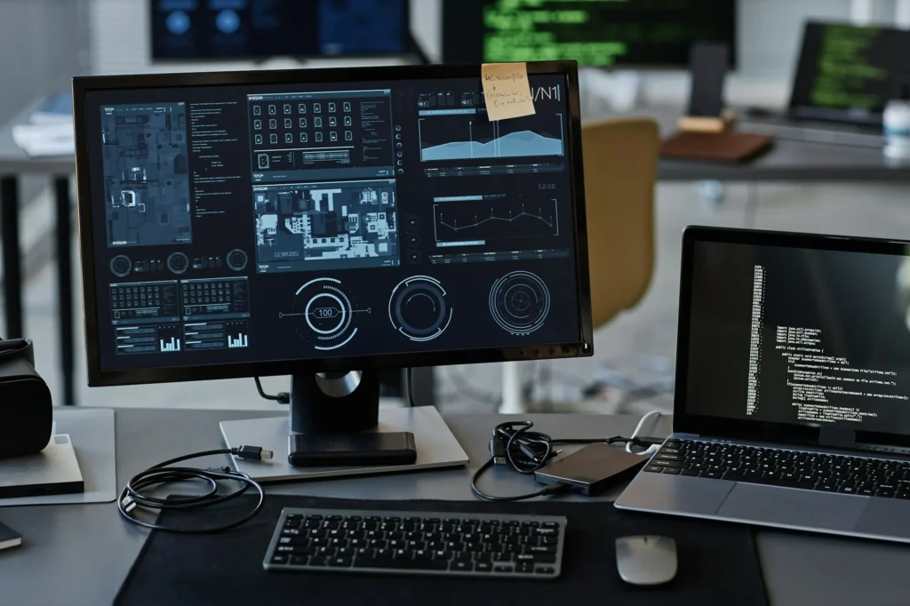 Computer workstation displaying software dashboards, analytics, and programming code.